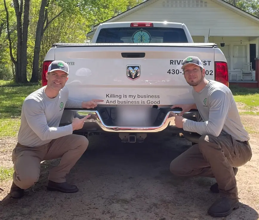 Two Rivers technicians crouched either side of a truck tailgate that reads Killing is my business, and business is good